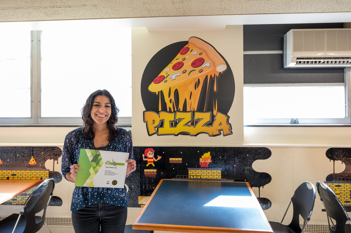 Karla Alvarado standing in Pete's Za near the environmental graphics that she designed.